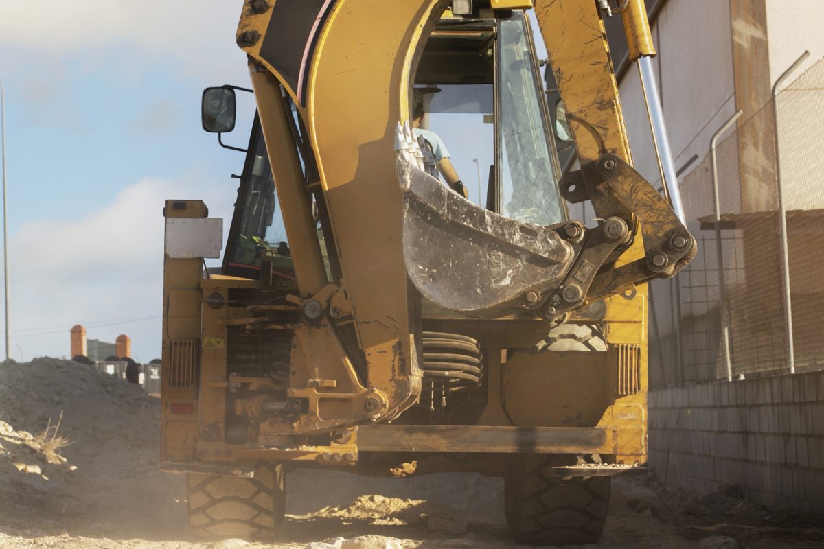 Backhoe with a worn bucket and hydraulic arm working a dusty construction road
