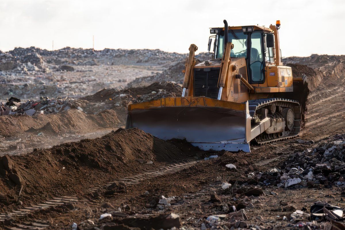 Yellow bulldozer pushing dirt and debris across a landfill site