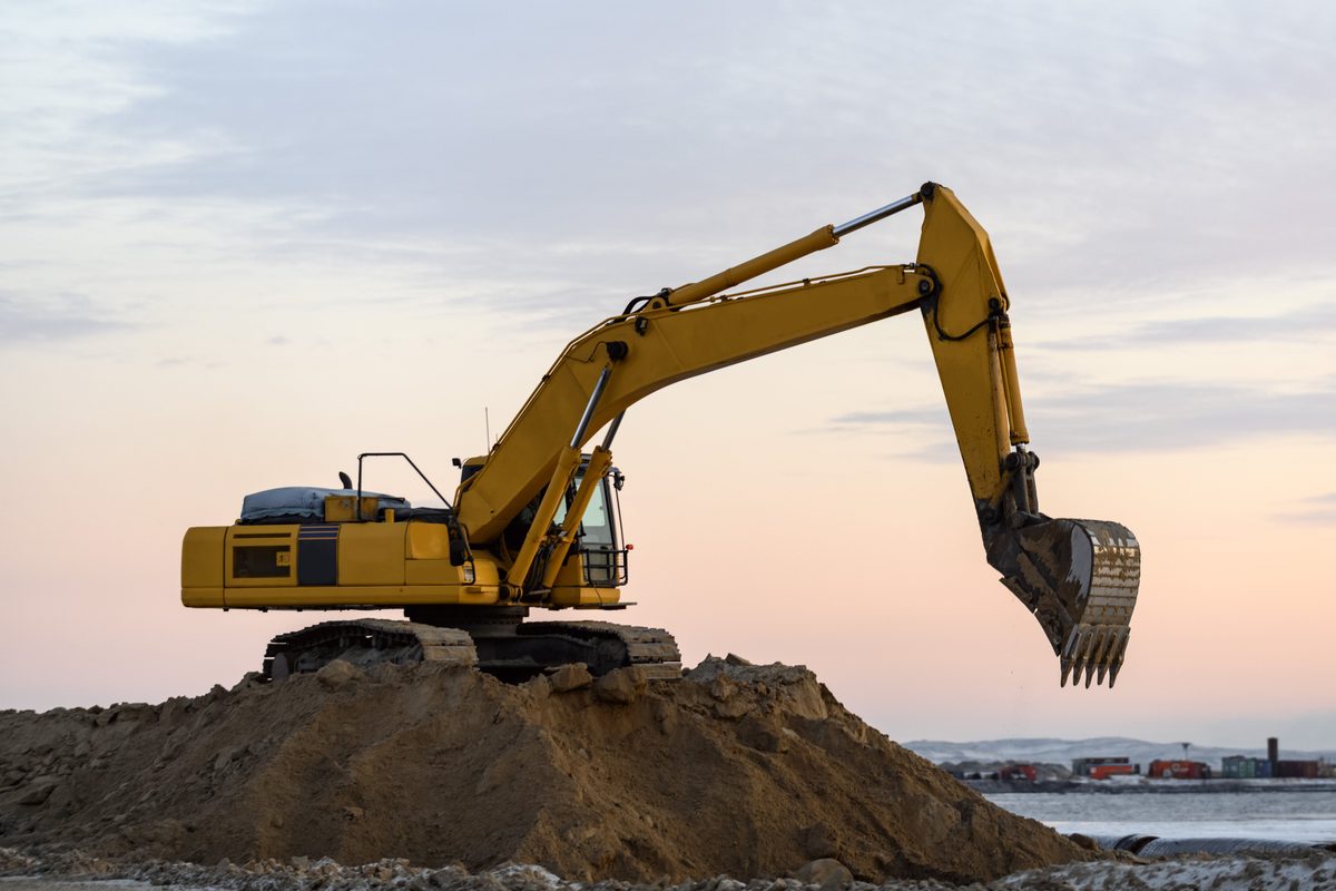 Yellow tracked excavator on a dirt mound at a construction site at dusk